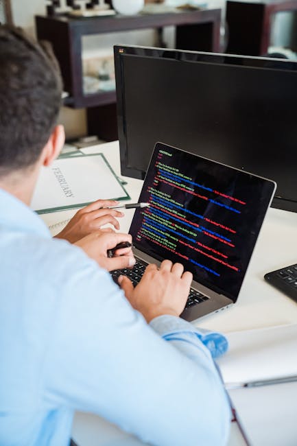 A close-up view of a laptop screen displaying lines of colorful code in a dark-themed IDE, positioned on a wooden desk. To the right of the laptop, there is a ceramic coffee mug with the phrase 'This